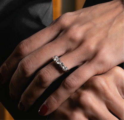 A close-up of two hands gently clasped, with one hand wearing an elegant lab-grown diamond eternity band. The ring sparkles under soft lighting, highlighting its brilliance against the natural skin tones and dark background.