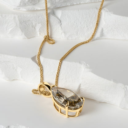 A close-up of a pear-shaped lab-grown yellow diamond pendant in a gold basket setting, resting elegantly on a textured white surface. The pendant is paired with a delicate gold chain, showcasing its intricate craftsmanship from a side angle.