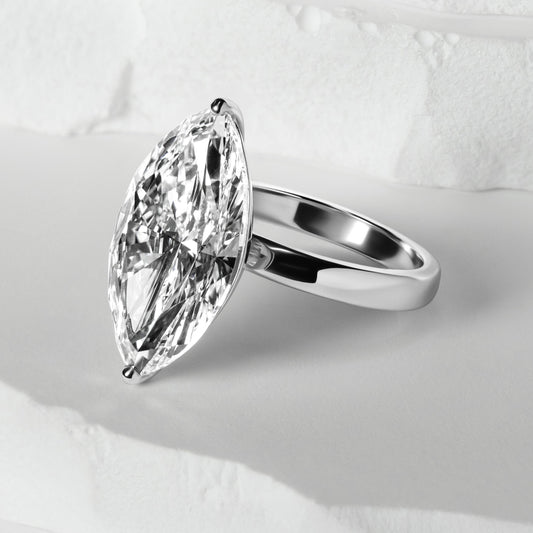 An elegant lab-grown diamond ring featuring an marquise-cut stone in a platinum band, showcased on a soft white surface with subtle textured accents, emphasizing its timeless beauty.