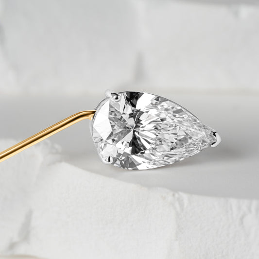 Close-up view of a pear-shaped lab-grown diamond set in a gold lapel pin, displayed against a white, textured backdrop that highlights its brilliance and clarity